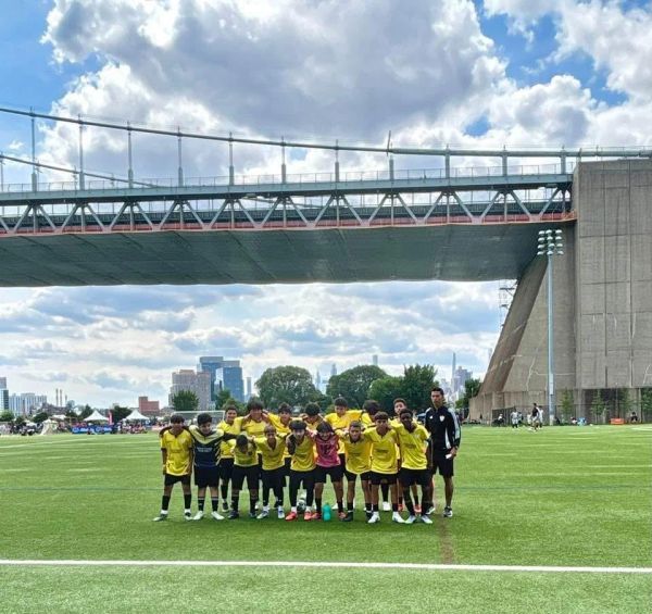 Youth soccer team posing on a green field under a large bridge.