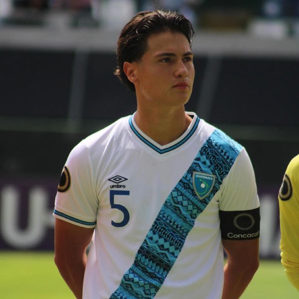 Guatemala soccer player wearing captain's armband and white jersey with blue diagonal stripe.