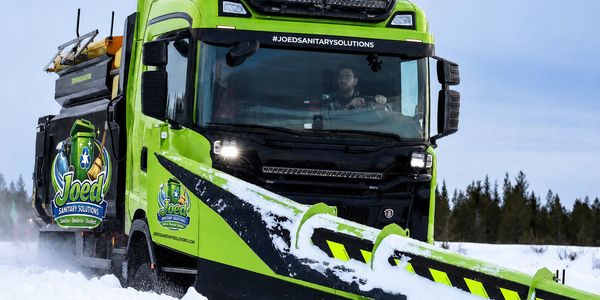 Green snowplow truck clearing snow on a winter road.