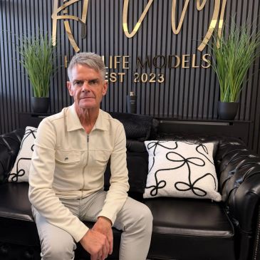 Man sitting on a black leather couch with decorative pillows.