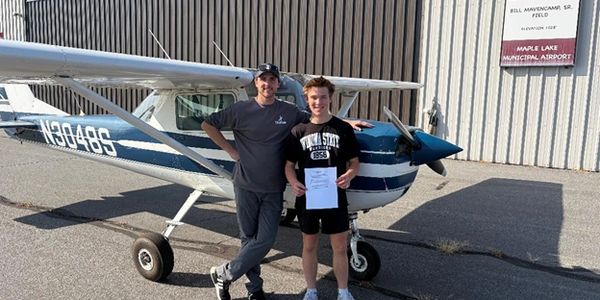 Two people standing next to a small airplane holding a certificate.