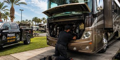 Mechanic repairs a motorhome engine outdoors at an RV park.