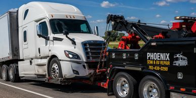 A tow truck towing a white semi-truck on a highway under a blue sky.