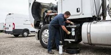 Mechanic performing maintenance on a large white truck outdoors.