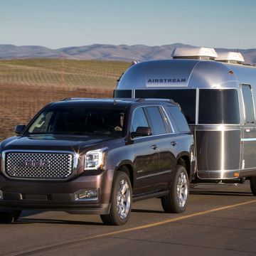 SUV towing a silver Airstream trailer on a road.