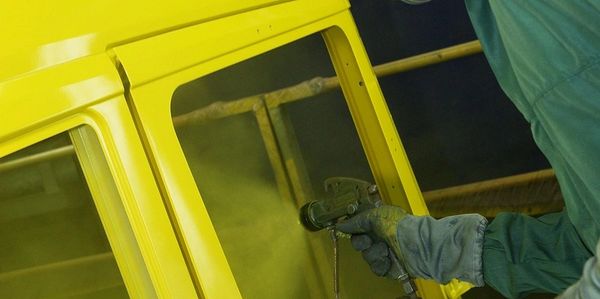 Worker spray painting a car body yellow with protective gear on.