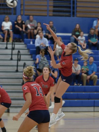 Female volleyball player jumps to hit the ball during a game in a gym.