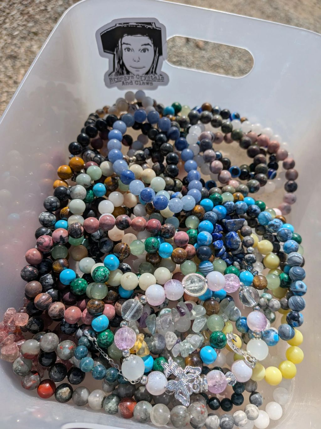 Colorful beaded crystal bracelets in a white container under sunlight.