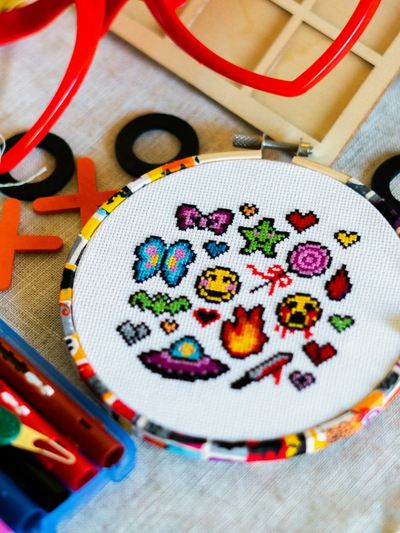 Colorful cross-stitch art with heart-shaped glasses and craft supplies.