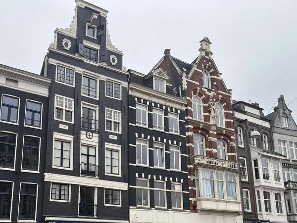 Historic canal houses with people walking and cycling on a cloudy day.