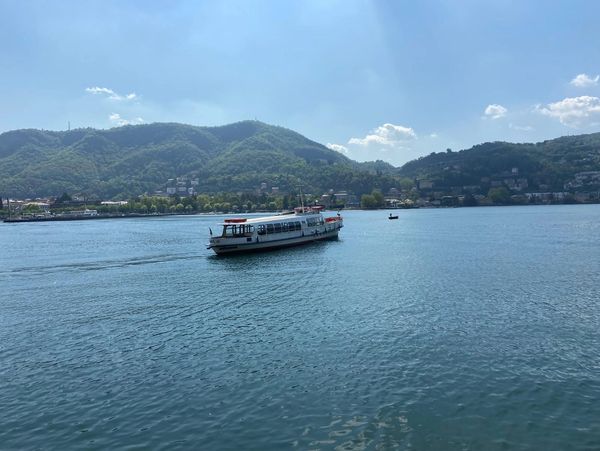 A passenger boat sailing on a lake with mountains in the background.