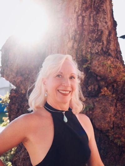 Smiling woman in black dress outdoors near a tree.