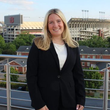 Woman in black suit smiling with stadium in background.
