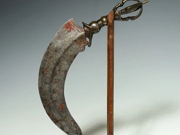 Antique curved blade weapon with ornate handle on a stand.