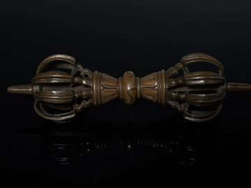 A bronze vajra with intricate design against a black background.