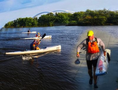 People kayaking and a man carrying fishing gear by the water.