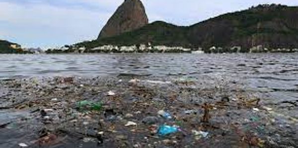 Polluted water body with floating trash and a mountain in the background.