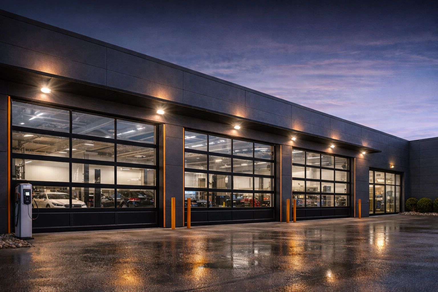 Modern car service center with glass garage doors lit at dusk.