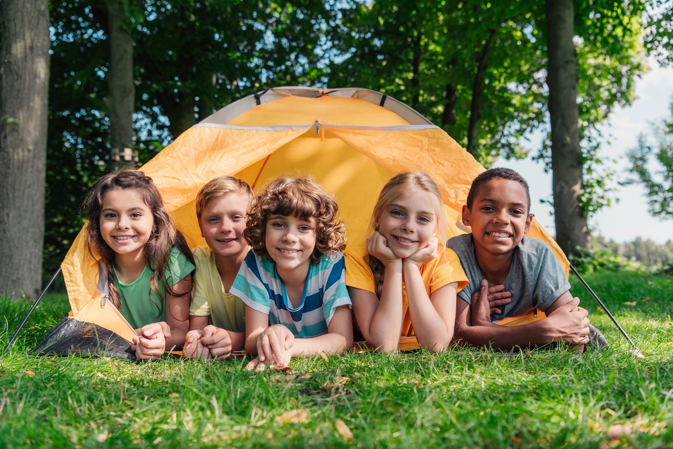 Five kids smiling in a tent outdoors.