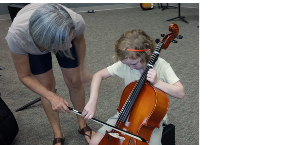 A young girl learning to play the cello with an instructor's guidance.