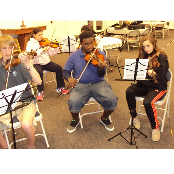 A group of young musicians playing violins indoors with music stands.