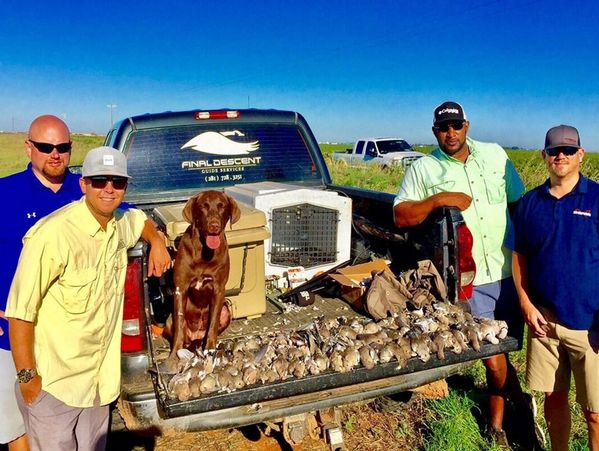 Four men and a dog with a pickup truck loaded with hunting gear and game birds.