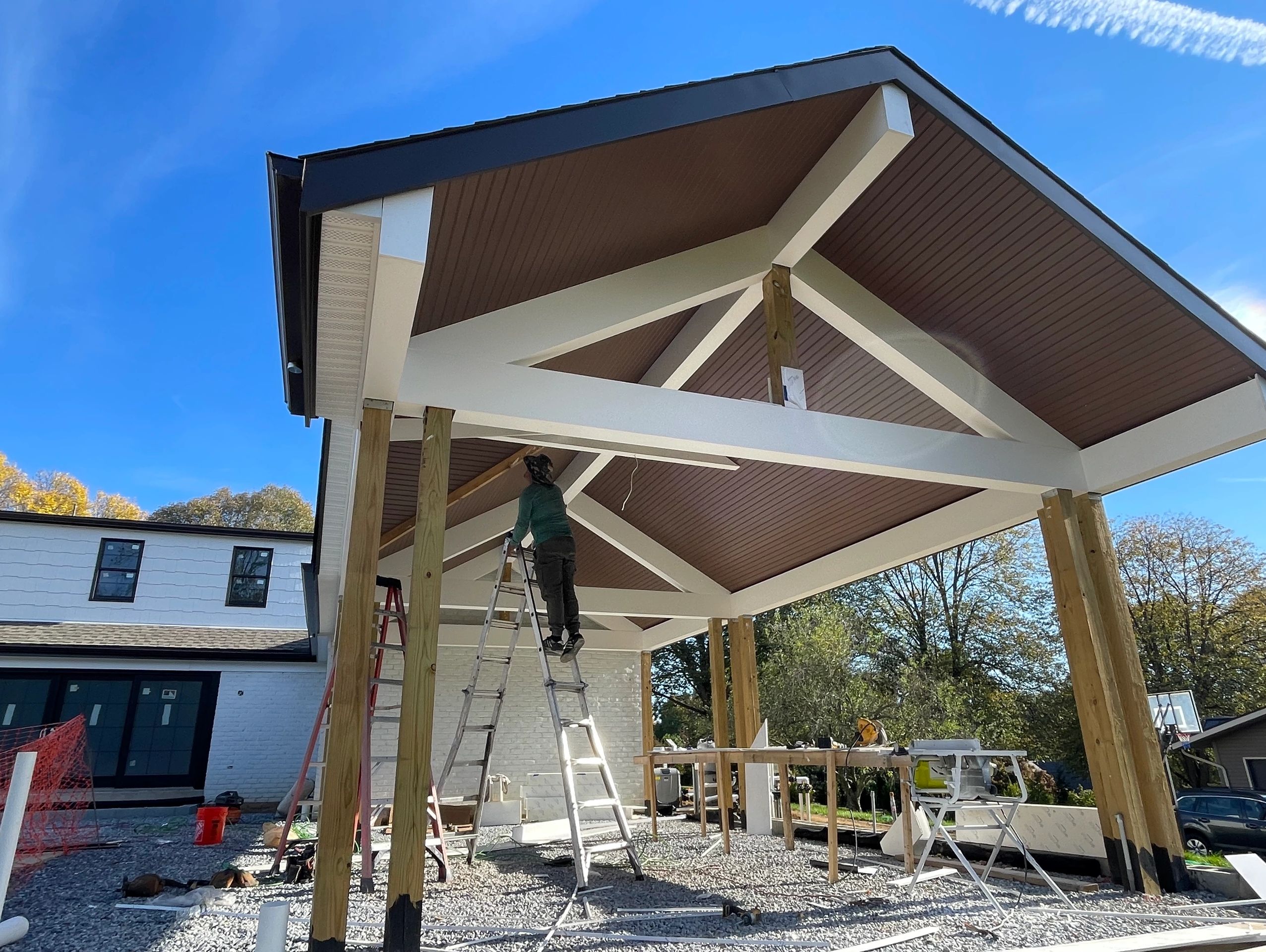 Construction worker installs roof beams on a modern carport under clear blue sky.