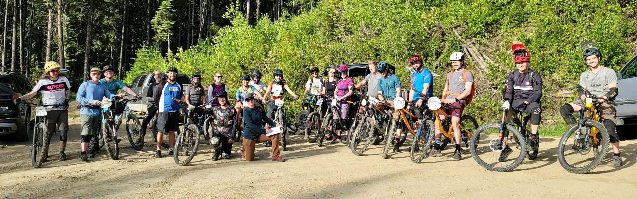 Group of mountain bikers posing with their bikes on a sunny forest trail.