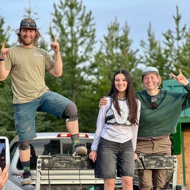 Three happy people posing on a truck bed outdoors.