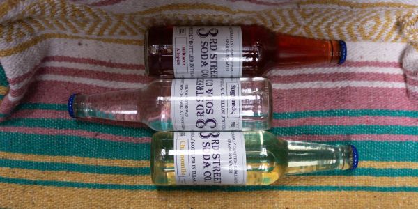 Three 3rd Street Soda Co bottles on a colorful towel.