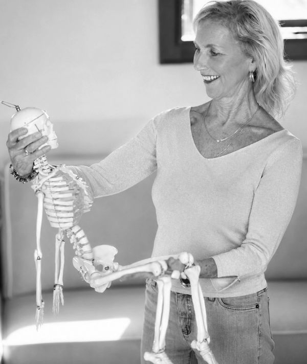 Smiling woman holding and examining a small human skeleton model.