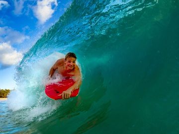 Man smiling on a large bodyboard, inside the curl of a wave, Beach Games Waikiki.