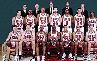 Photo of a basketball team with players and coaches in Bulls uniforms, celebrating their strategy.