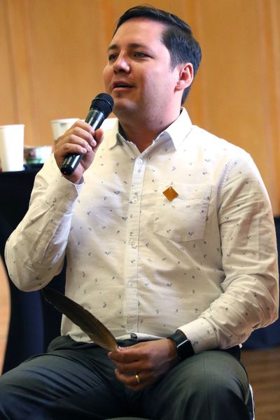 Photo of Jordan Wapass holding a microphone and a feather, speaking about Indigenous strategy.