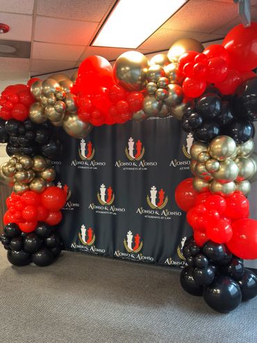 Decorative balloon arch with red, black, and gold balloons at a law office.