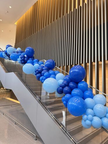 Blue balloon garland decorating an escalator in a modern building.