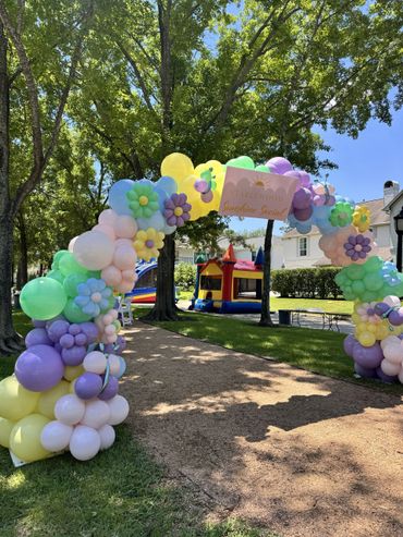 Colorful balloon arch with flowers at an outdoor party.