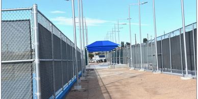 A pathway between chain-link fences with a blue canopy in the distance.