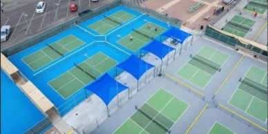 Aerial view of multiple tennis courts with blue shade structures.