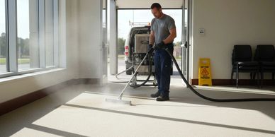 A man steam cleans a carpet in a bright room.