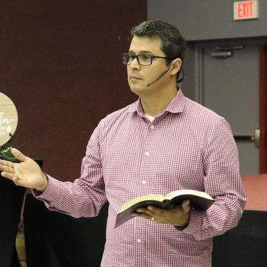 Man speaking with a headset and holding an open book.