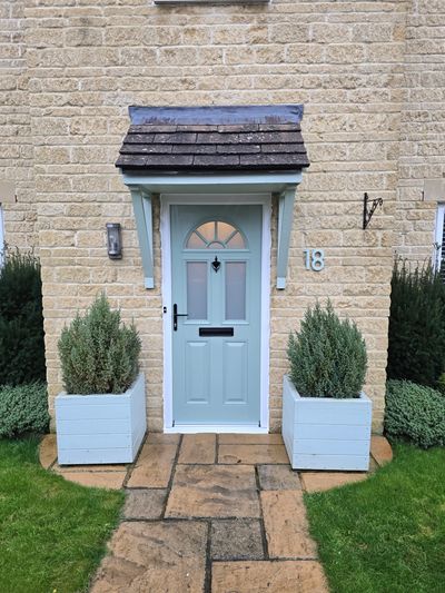 A light blue front door with two potted plants and stone pathway.