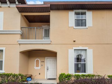 Two story condo with yellow stucco and a white front door. Balcony with iron railing on the second l