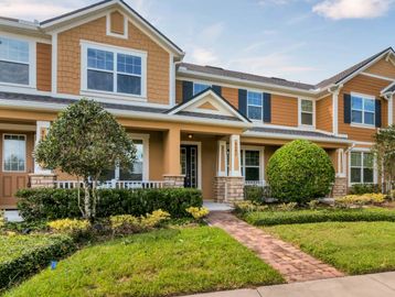 Yellow stucco town home with covered front porch and white railing. Paver walkway and green grass.