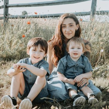 Woman with two young boys sitting outdoors in a field.