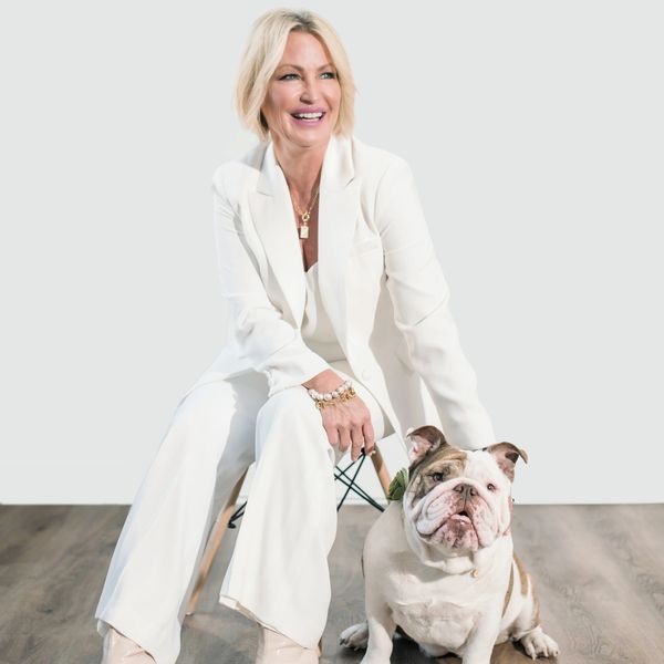 Woman in white suit sitting with a bulldog on a wooden floor.