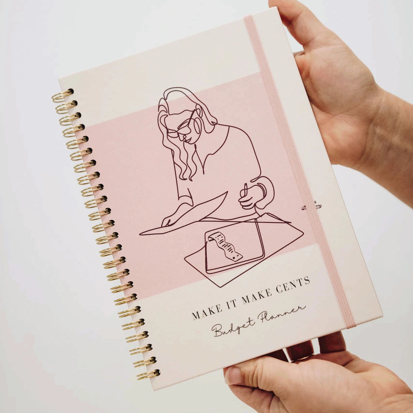 Person holding a pink budget planner with a line art design on the cover.