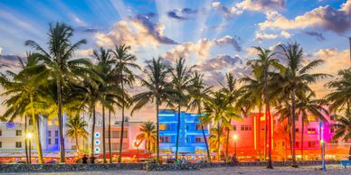 Palm trees in front of colorful art deco buildings at sunset.