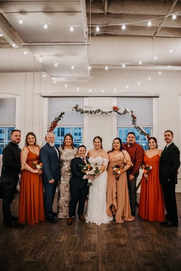 A wedding group photo with the couple at the center and bridesmaids and groomsmen on either side.