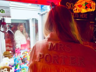 Woman in a "MRS PORTER" jacket playing a claw machine game.
